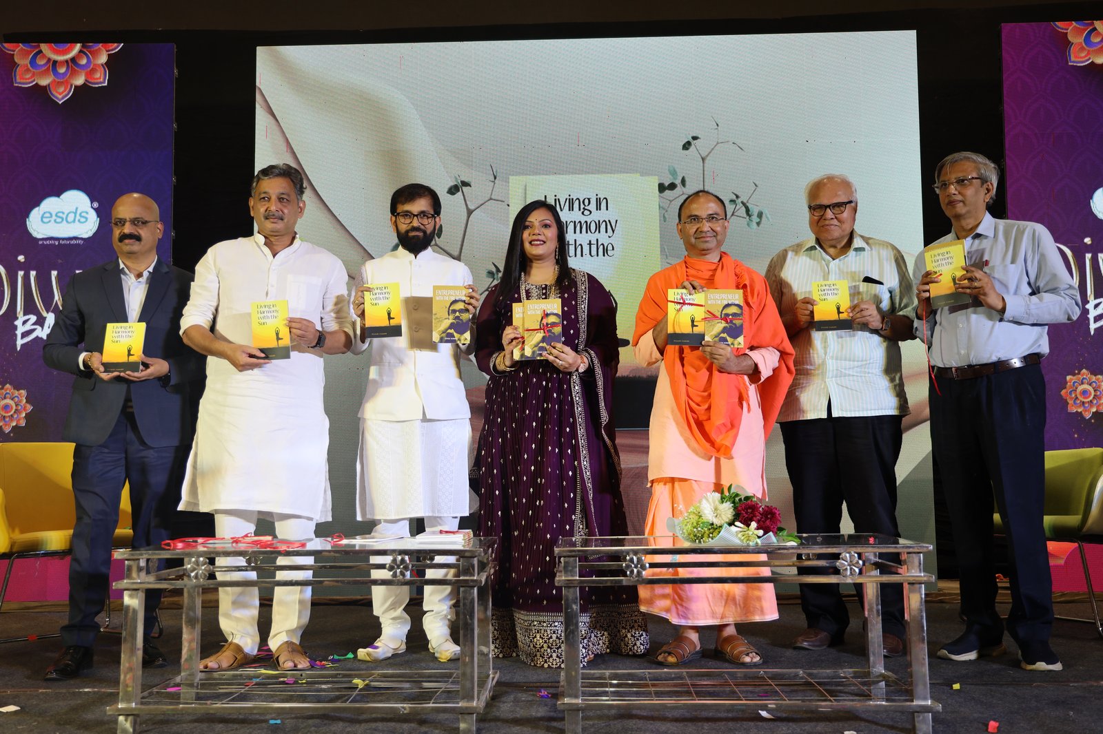 Book launch event with seven dignitaries on stage holding both books